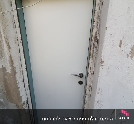 דלת לבנה עם ידית מתכת במסגרת קיר מתקלף
